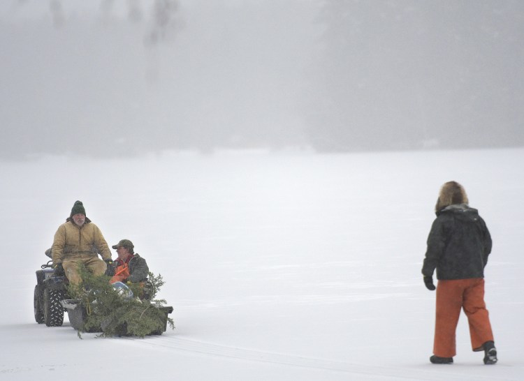 Men venture onto Cochnewagon Lake in Monmouth on Monday using an all-terrain vehicle and by foot. A recent cold snap has created a narrow shelf of ice on several shallow bodies of water across central Maine. The crew was erecting poles to mark snowmobile trails on the lake.