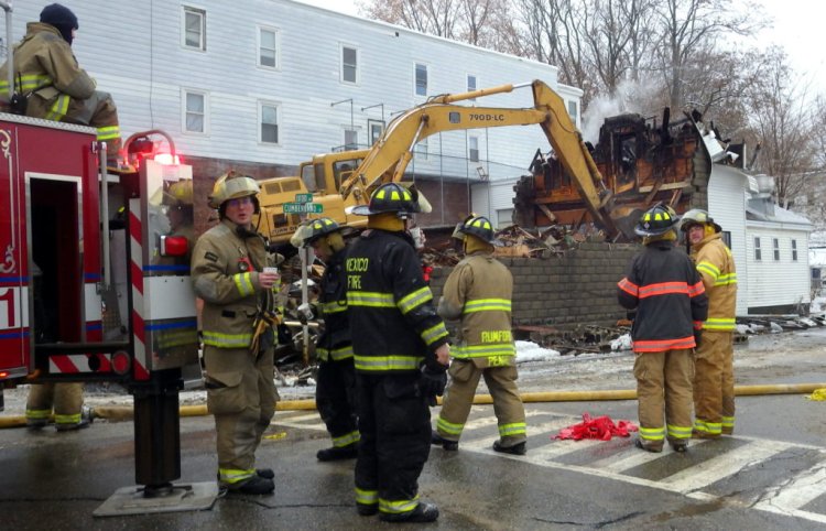 After battling an early morning fire Tuesday at the corner of Oxford Avenue and Cumberland Street in Rumford, firefighters watch an excavator tear down the burnt portion of the unoccupied building. 