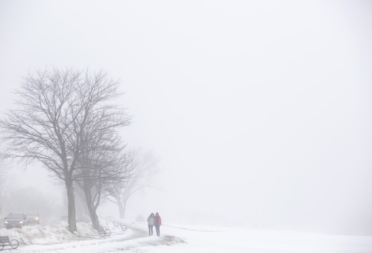 Kerri Smith and Allison Keely, right, both of Portland, tread carefully on a path along the Eastern Promenade, which is shrouded in fog from the melting snow Friday. Cold temperatures are expected to return this weekend.