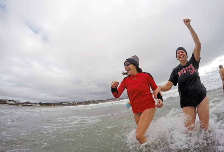 Above, Abraham Boulter, center, of Sanford, bounds into the frigid water at Kennebunk's Gooch's Beach on Saturday morning for the 17th annual Atlantic Plunge. At top, Diana Onacki, right, with her unidentified plunge partner, raises her hand in victory after emerging from the 41-degree water. The event benefits a York County center for victims of abuse.