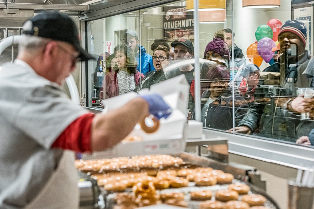 Customers watch the hot doughnuts coming off the line at Krispy Kreme in Auburn during the grand opening Monday morning. People waited outside in the cold for as long as 15 hours before the store switched on its "Hot Now" light at 6 a.m. ..