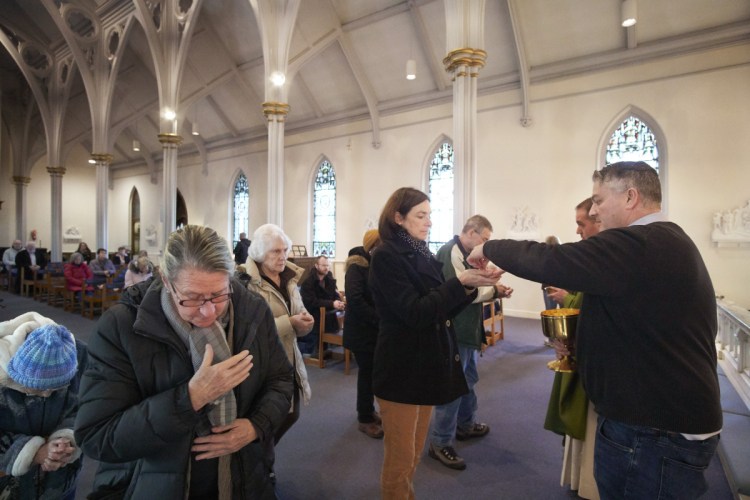 Eucharistic Minister Peter Doyle, right, serves communion Thursday during Mass at the Cathedral of the Immaculate Conception in Portland, placing the wafer into Carolyn Willard's open palms. As the flu season worsens, the Roman Catholic Diocese of Portland and other religious authorities have recommended altering some Mass protocols, such as handshakes during the Sign of Peace, to limit exposure to germs.