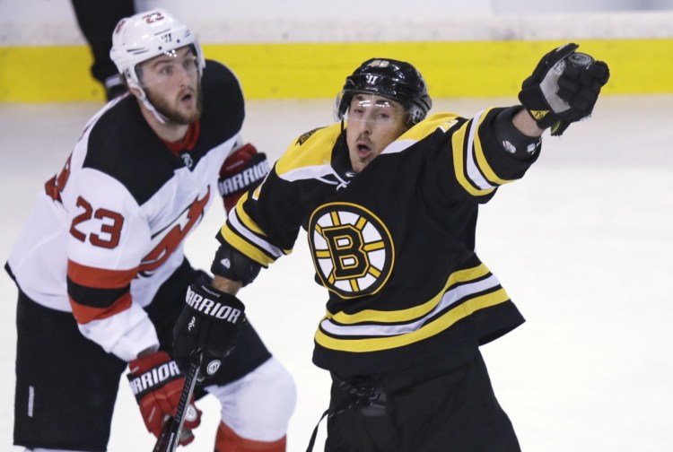 Boston's Brad Marchand reaches for the puck next to New Jersey's Stefan Noesen in the first period Tuesday night in Boston. Marchand had a goan and an assist as the Bruins beat the Devils, 3-2.