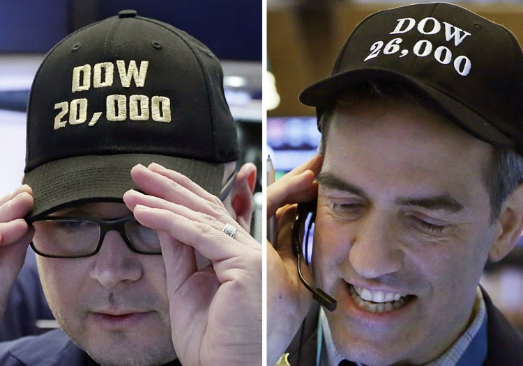 Specialist Mario Picone, left, adjusts his Dow 20,000 cap on Jan. 25, 2017, and trader Gregory Rowe wears a Dow 26,000 cap nearly a year later on Jan. 16, 2018, at the New York Stock Exchange.