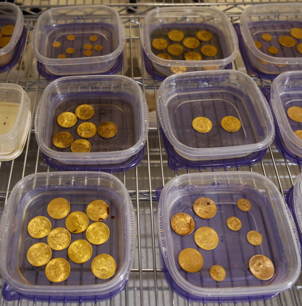 Rust-covered gold coins sit in containers of water while being restored.
