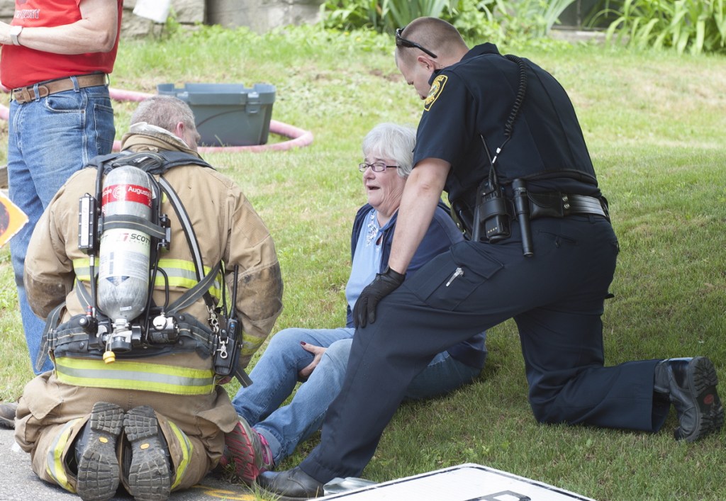 Augusta Firefighter Dave Groder, left, and Augusta police Officer Brad Chase attend to Rebecca Poulin as she watches firefighters put out a fire in the kitchen of her home at 65 School St. in Augusta on June 24, 2015.