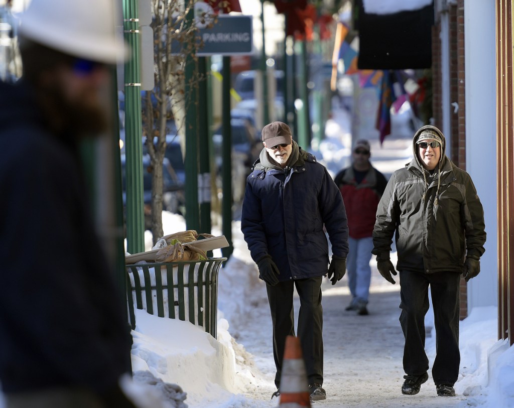 People walk along Water Street on Wednesday in Gardiner with high snowbanks lining the sidewalk.