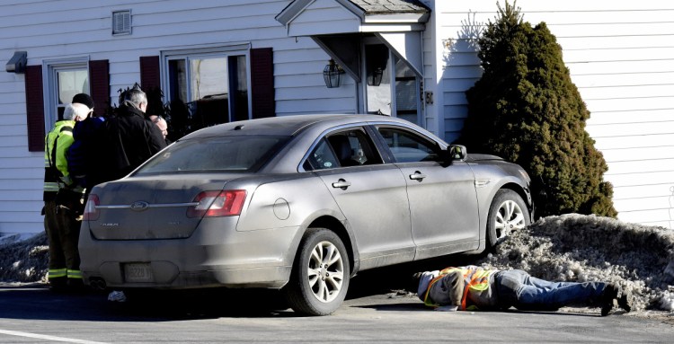 A tow truck operator looks under a vehicle that struck 50 Halifax St. in Winslow after the driver reportedly lost control of the vehicle Wednesday.