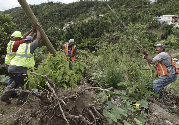 Four months after  Hurricane Maria hit Coamo, Puerto Rico, a public works official, in hardhat at left, and others install a power pole. Volunteers and municipal workers have installed more than 60 poles in Coamo.