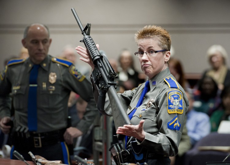 Firearms training unit Detective Barbara J. Mattson, of the Connecticut State Police, holds up a Bushmaster AR-15 rifle, the same make and model of gun used by Adam Lanza in the Sandy Hook School shooting, during a hearing of a legislative subcommittee in Hartford, Conn. Remington, the gunmaker beset by falling sales and lawsuits tied to the Sandy Hook Elementary School massacre, said Monday that it has reached a financing deal that would allow it to continue operating as it files for Chapter 11 bankruptcy protection.