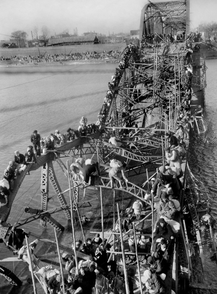 Fleeing refugees crawl perilously over the shattered girders of a bombed bridge in Pyongyang, North Korea, in a photo taken by Max Desfor. The renowned photographer died this week at age 104.