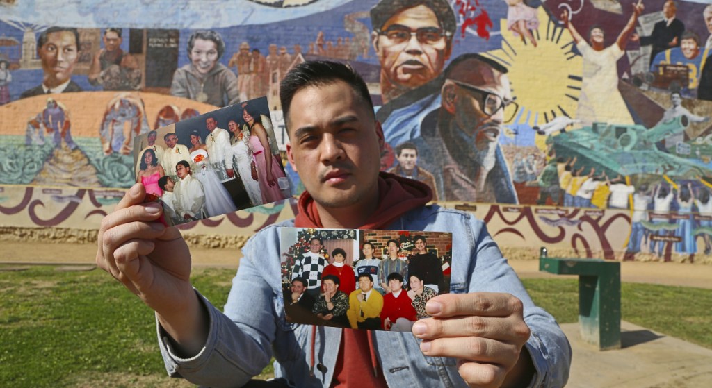 Filipino American Jeff DeGuia holds up family pictures at Unidad Park in Los Angeles earlier this month. DeGuia, 28, says it took his mother more than a decade to bring two sisters from the Philippines.