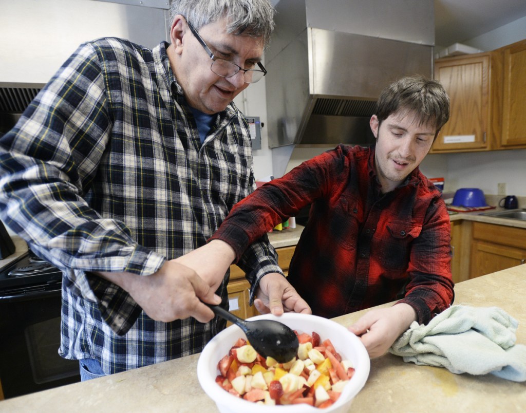 David Conrad helps Brendan Young make a fruit salad in cooking group at STRIVE in South Portland. A bill in the Legislature to stabilize the group home workforce would cost $26 million a year.