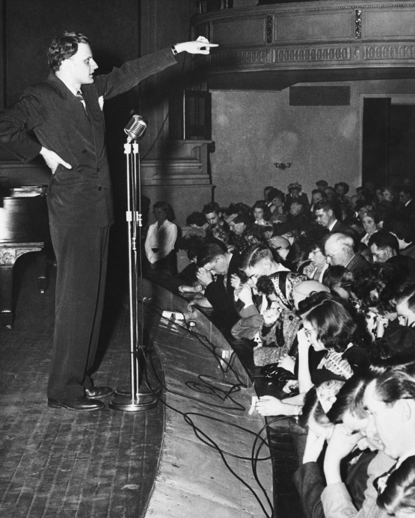 Billy Graham gestures as several hundred people answer the call to have their souls "cleansed of sin" at a rally in City Hall Auditorium in Portland on March 28, 1950, as he launched his New England tour.
