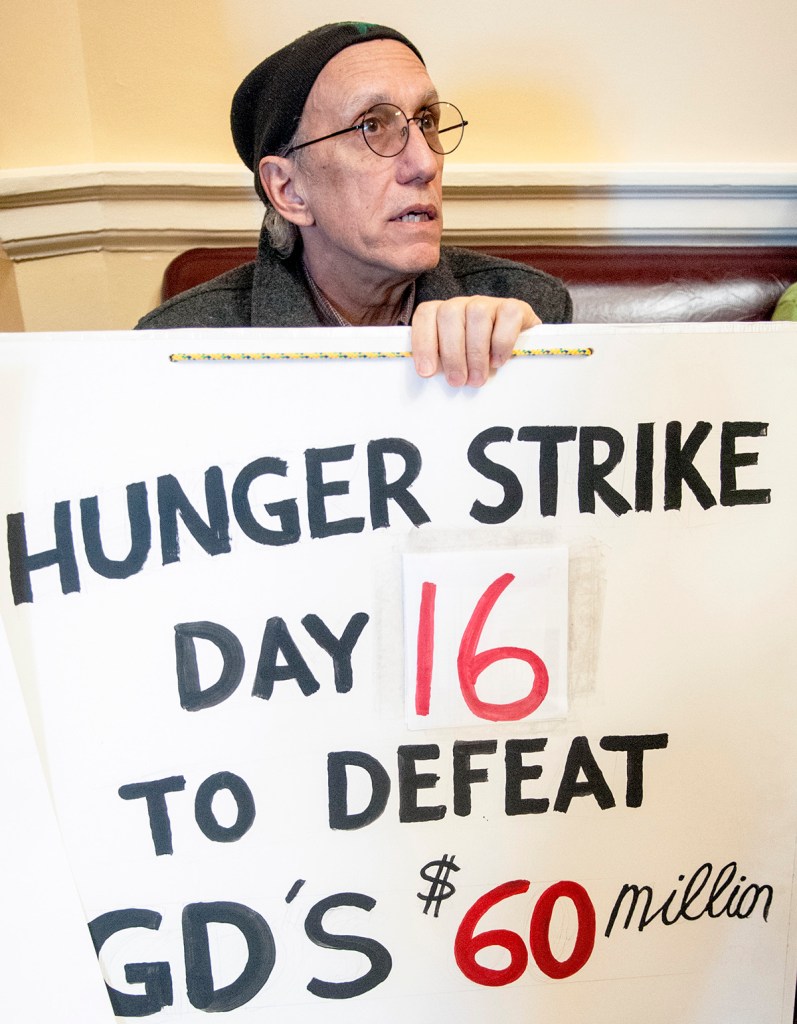 Bruce Gagnon, of Bath, holds his sign opposing Bath Iron Works' tax credits last month at the State House. Gagnon was on the 16th day of a hunger strike.