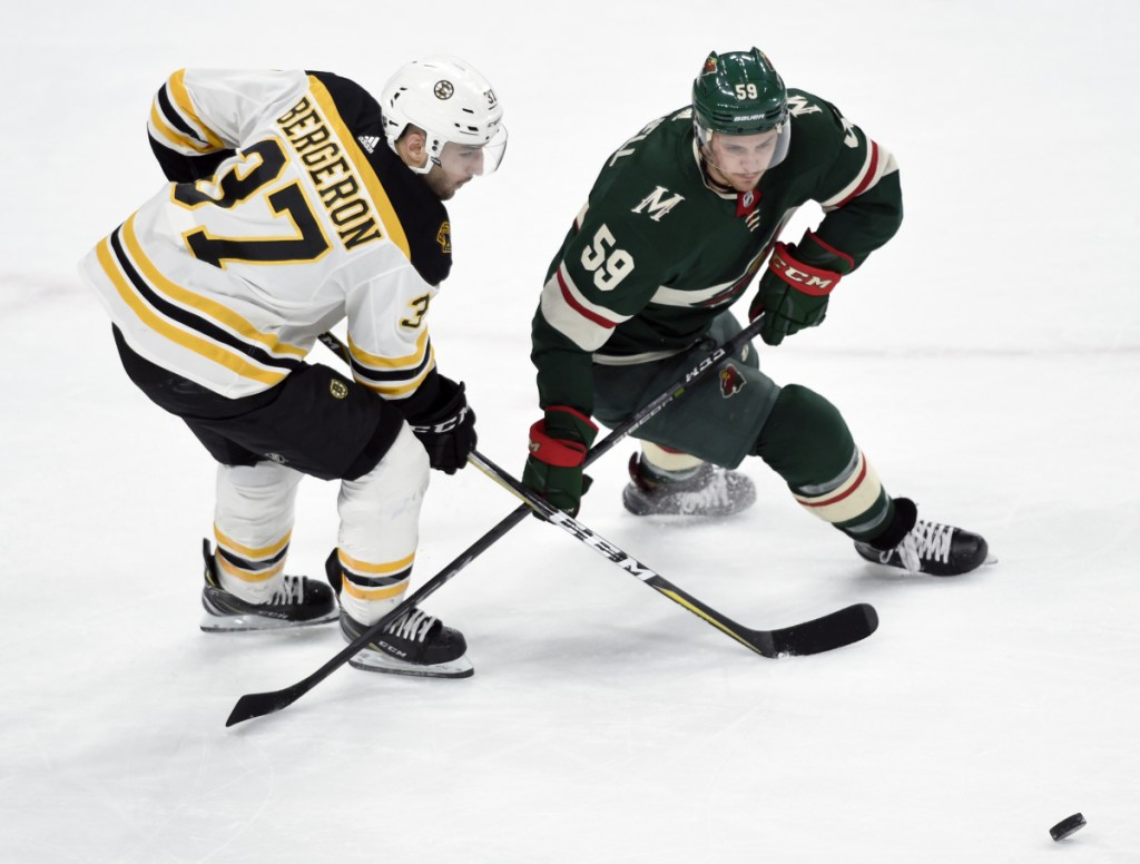 Patrice Bergeron of the Bruins battles for the puck with Minnesota's Zack Mitchell during Sunday's game in St. Paul, Minn. The Bruins won in overtime, 2-1.