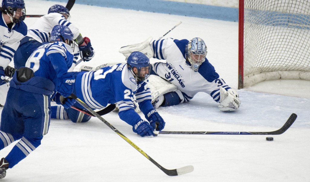 Colby College's Phil Klitirinos (23) is taken down in front of the University of New England net as Nor'easters goalie Tate Sproxton tries to recover during the first period Saturday of a NCAA Division III first-round tournament game at Harold Alfond Forum in Biddeford.