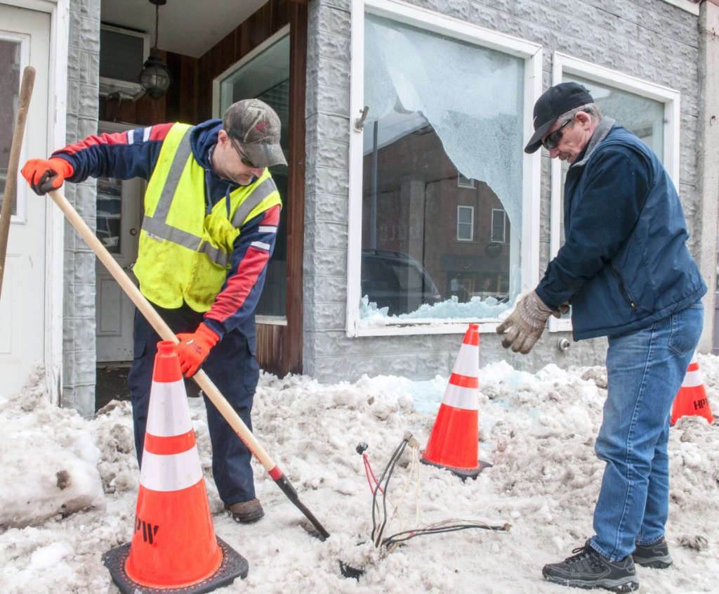 Todd Talon, left, of the Hallowell Public Works Department, scrapes snow away from the base of a broken light pole as Dick McGibney, of Dick's Electrical Service, prepares to wrap up wires Thursday. They were cleaning up after a tractor-trailer truck hit the streetlight and broke a window at 108 Water St. in downtown Hallowell.