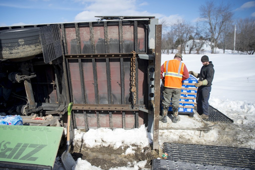Crews carefully stack a tractor-trailer's payload of beer on pallets for transfer to another truck Friday after the first one rolled over on Trafton Road in Waterville when it hit a soft area on the road's shoulder.