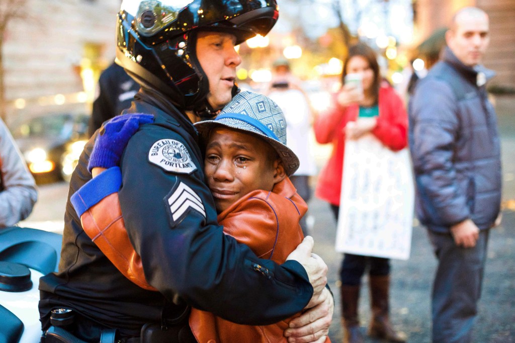 In this Nov. 25, 2014, file photo provided by Johnny Nguyen, Portland police Sgt. Bret Barnum, left, and Devonte Hart, 12, hug at a rally in Portland, Ore., where people had gathered in support of the protests in Ferguson, Mo. 