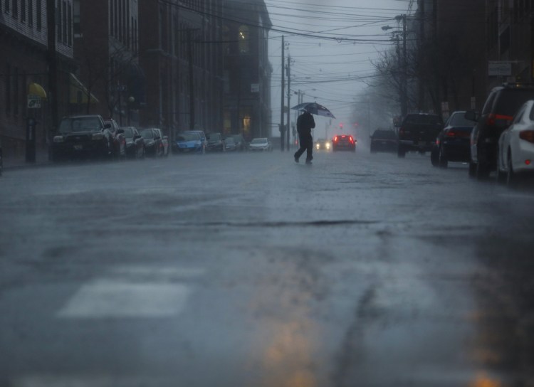 A man crosses Pearl Street in the rain on Monday. There were widespread power outages and flooded roads from the storm.