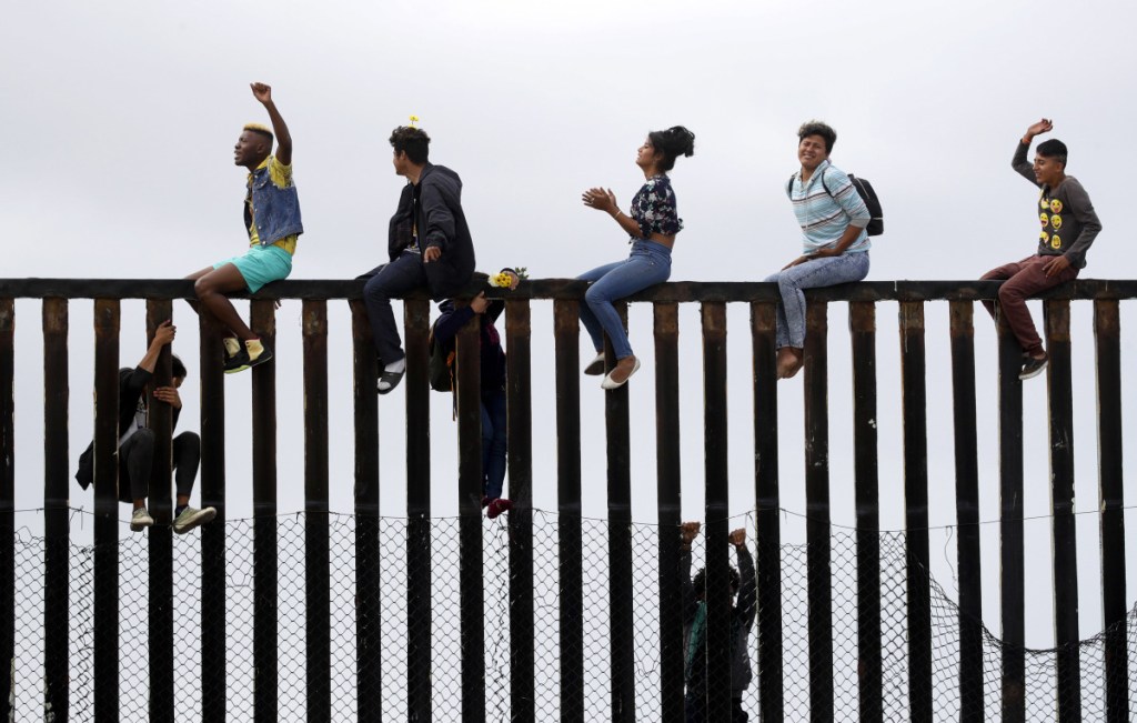 Central American migrants sit on top of the border wall on the beach in San Diego during a gathering of migrants living on both sides of the border Sunday.