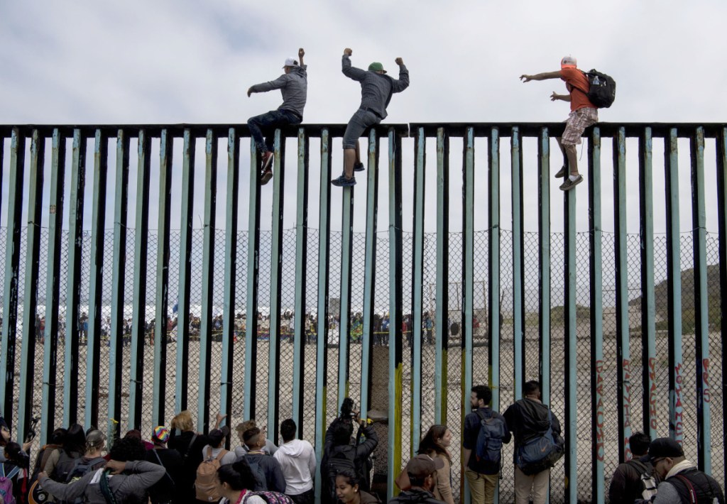 Central American migrant families and activists gather Sunday at the border fence in Tijuana, Mexico, as some climb to the top.