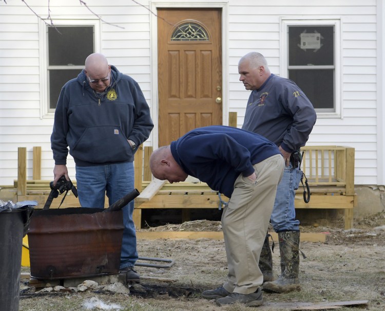 Office of State Fire Marshal investigator Ken MacMaster, left, Winthrop Fire Chief Dan Brooks and Winthrop firefighter Mark Arsenault inspect a burn barrel Tuesday outside a residence in Winthrop, where Leon Deblois suffered leg burns.