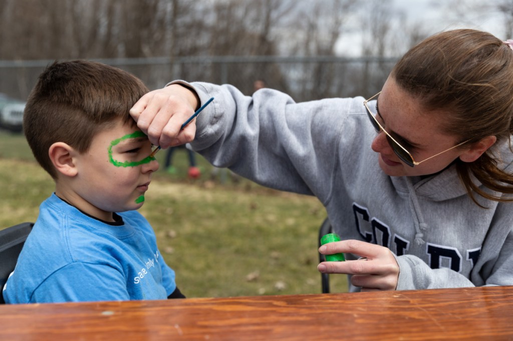 Sarah Taft, co-director of the Volunteer Center at Colby College, paints a snake Saturday onto the face of Gideon McGee, of Waterville, during Colby Cares Day at Couture Field on Water Street, where a public lunch was served after students finished their morning service projects.