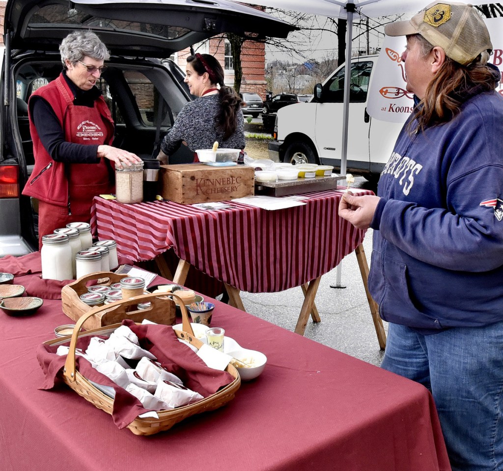 Jean Koons, left, and Caroline Ham, of the Kennebec Cheesery, set up their booth as Debbie Ferguson of Snakeroot Organic Farm samples cheese on Thursday. The Downtown Waterville Farmers' Market has opened for the season on Common Street in Waterville and will have products for sale every Thursday.