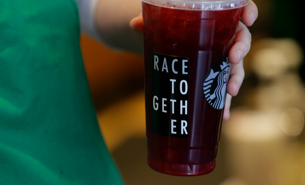 A Starbucks barista holds an iced tea drink with a "Race Together" sticker on it on March 18, 2015, at a Starbucks store in Seattle. Three years ago, Starbucks was widely ridiculed for trying to start a national conversation on race relations by asking its employees to write the words “Race Together” on coffee cups. The initiative, though it backfired, was in line with the company’s longstanding effort to project a progressive and inclusive image. 