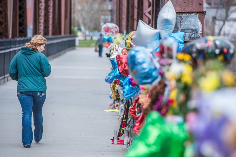 Brenda Card-Burmeister observes the tribute Monday morning on the Simard Payne Pedestrian Bridge. The tribute of stuffed animals, flowers and balloons has been growing steadily as the search continues for the 5-year-old boy who was swept away last week in the Androscoggin River. 