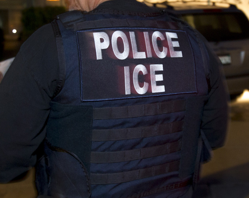 In this March 30, 2012 photo, an Immigration and Customs Enforcement (ICE) agent waits with other agents outside of the home of a suspect before dawn as part of a nationwide immigration sweep in San Diego. Federal officials say they arrested more than 3,100 immigrants convicted of serious crimes and fugitives in a six-day nationwide sweep. Officials at U.S. Immigration and Customs Enforcement say the sweep included every state and involved more than 1,900 of the agency’s officers and agents.  (AP Photo/Gregory Bull)