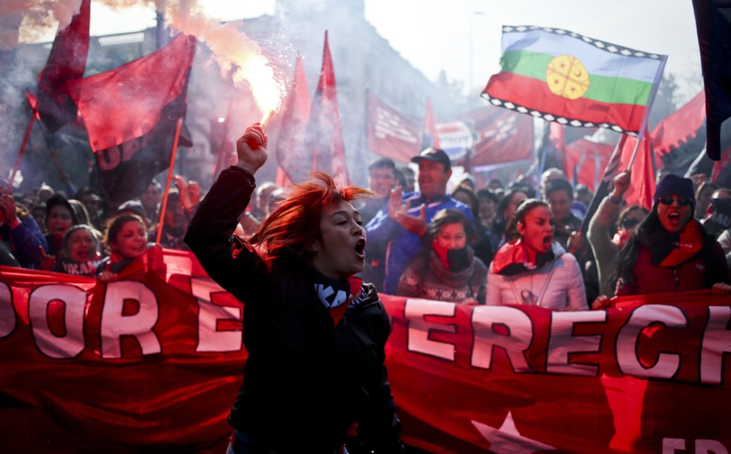 Above, a woman holds a flare as a crowd demands that the government address labor issues during the annual May Day march Tuesday in Santiago, Chile. Below, people march in the center of Barcelona, Spain.