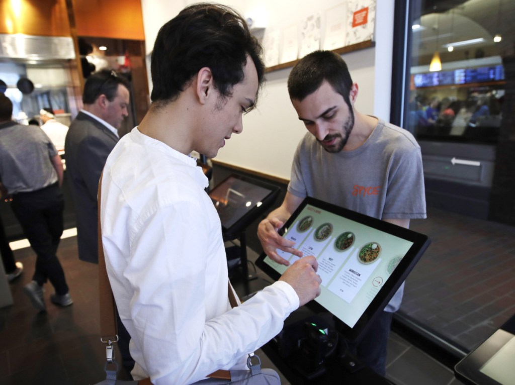 Charles Renwick, right, lead software engineer at Spyce Food Co., assists a customer with an order at the Spyce restaurant. It was founded by four former MIT classmates who partnered with Michelin-starred chef Daniel Boulud.