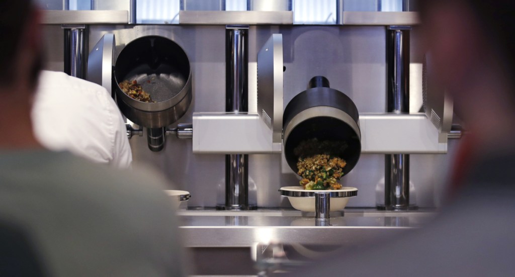 Customers wait as their automatically prepared food is dropped from a cooking pot into a bowl at Spyce restaurant. Other eateries marketing themselves as powered by robots or automation have grabbed attention from first-time customers in recent years, but usually haven't lived up to the hype.