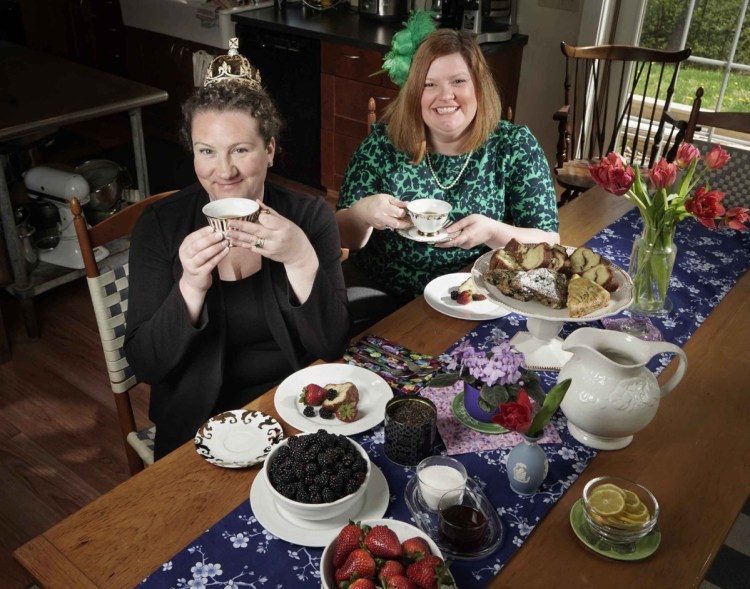 Karen Sigler, left, wearing a crown, and Kristin Fuhrmann-Simmons, wearing a fascinator, with some of the kinds of food and beverages Fuhrmann-Simmons plans to serve at a bash at her home on the morning of the royal wedding.