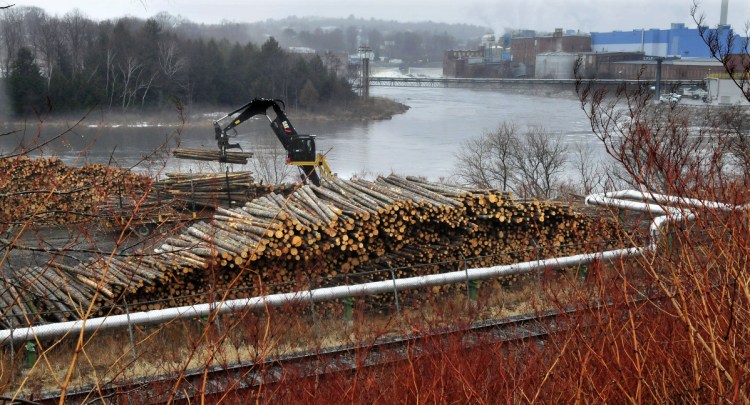 A worker unloads logs March 15, 2016, in a wood yard. The logs would be used to make paper at the Madison Paper Industries mill, in the background.