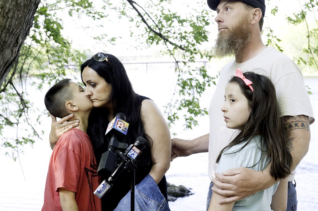 Maxim McFarland, 10, gives his mother, Helena Gagliano-McFarland, a kiss while his father, Jason McFarland, holds his sister, Giada, 9, on the side of the Androscoggin River in Auburn on Wednesday. Maxim and his brother, Valerio, fell into the river April 24. Maxim was rescued soon after while his 5-year-old brother's body was found nearly three weeks later.