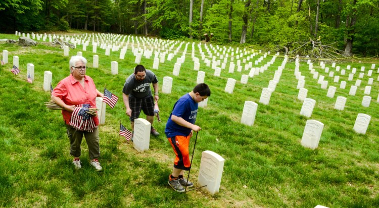 Sue Colfer, left, and Michael Simon walk along and put American flags the holes Elijah Simon is making with an L-shaped metal tool on Friday in one of the two sections of the Togus National Cemetery. About 75 volunteers set out flags on the about 5,400 graves ahead of Memorial Day on Monday. All of the graves received American flags and Medal of Honor winners also got a special blue flag.