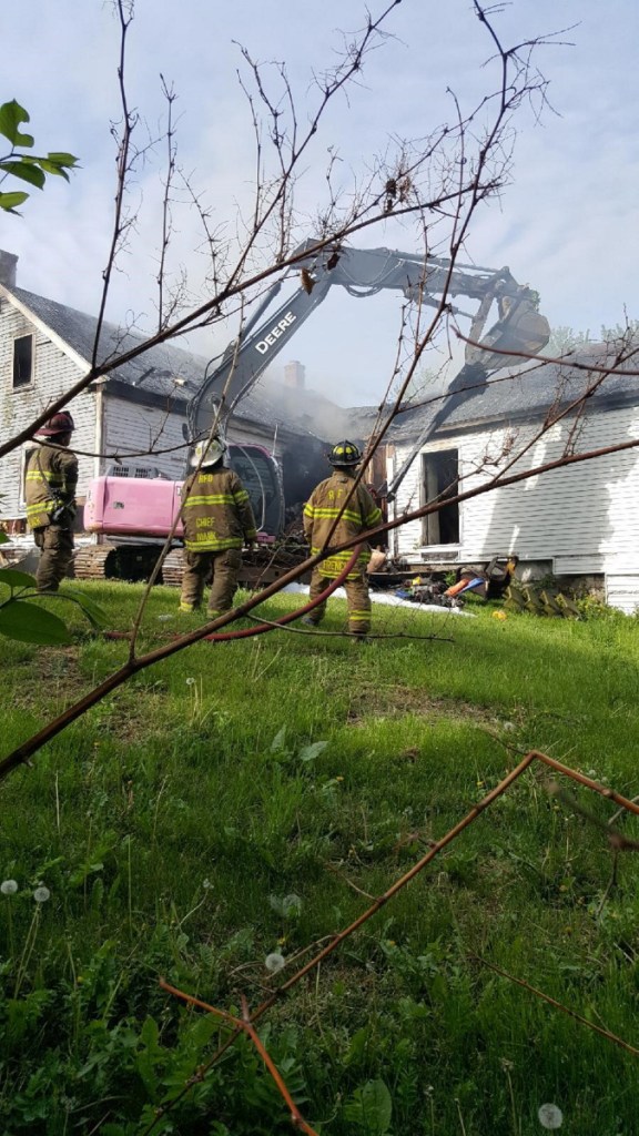 An excavator knocks down the front of the home at 114 Belgrade Road Sunday morning, as firefighters attack the fire that broke out there around 4 a.m.