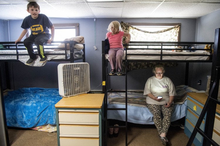 Jennifer Sweetster, bottom right, looks at her phone from her bunk as her daughter Hannah Chapman, 5, top right, and son Keith Chapman, 9, left, sit on their bunks at the Western Maine Homeless Outreach shelter in Farmington on Wednesday.