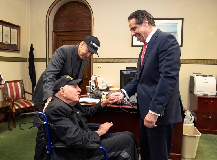 In this photo provided by the Office of the Governor of New York, Governor Andrew M. Cuomo, right, shakes hands with World War II veteran Sidney Walton at the Capitol in Albany, N.Y., Friday, May 18, 2018. The 99-year-old World War II veteran who regretted skipping the chance to meet some of the nation's last Civil War veterans in 1940 is on a mission to visit all 50 states so people who've never met a WWII vet can finally meet one. Standing at left is Walton's son, Paul Walton. 