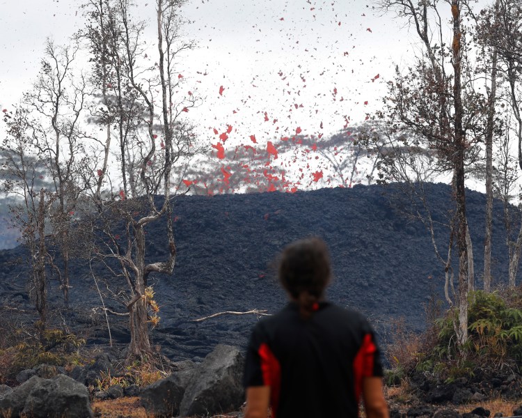 Abe Pedro watches lava shoot out of a fissure on Pohoiki Road, Friday, near Pahoa, Hawaii. Hawaii residents covered their faces with masks after a volcano menacing the Big Island for weeks exploded, sending a mixture of pulverized rock, glass and crystal into the air in its strongest eruption of sandlike ash in days.