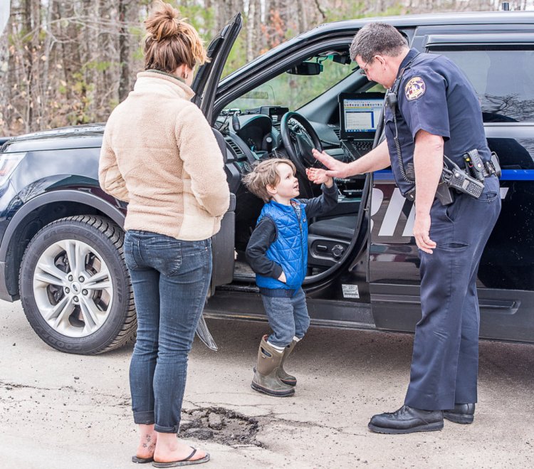 Androscoggin County Sheriff's Deputy Dennis Sampson gives a low-five to 5-year-old Sebastian Coron in Poland last Monday. Left is Angela, Sebastian's mother, asking Sampson about a fire on Cobb Road. 