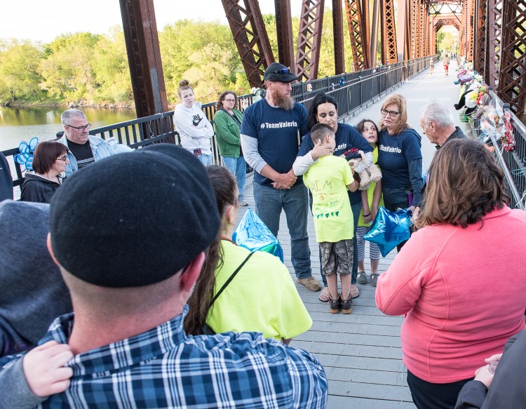 Maxim McFarland, 10, is comforted Thursday evening by his mother, Helena Gagliano-McFarland, while his father, Jason McFarland, left, looks on during a public vigil on the walking bridge over the Androscoggin River in Auburn. The remembrance was held near where 5-year-old Valerio McFarland fell into the river last month. Giada McFarland, 9, at right, hugs family friend Robin Schmidt as Schmidt addresses the gathering.