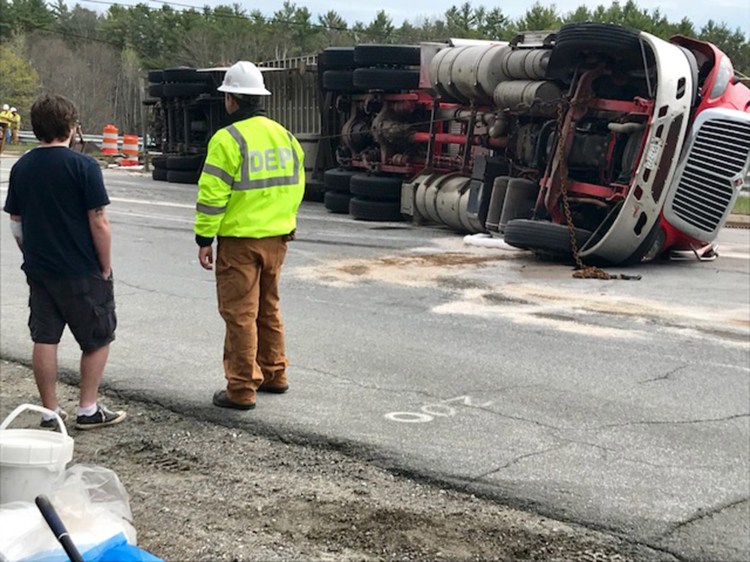 The driver of an overturned tractor-trailer, and personnel from the state Department of Environmental Protection, stand near the wreck just off the southbound exit off Interstate 295 on the Falmouth Spur on Friday afternoon. The driver, who refused to identify himself, citing company policy, appeared to have suffered only cuts on his left arm. The truck, which had Prince Edward Island tags and bore the company name Bulk Carriers, was carrying a full load of peat moss, which had to be unloaded before the truck could be righted because the weight would break the trailer. 