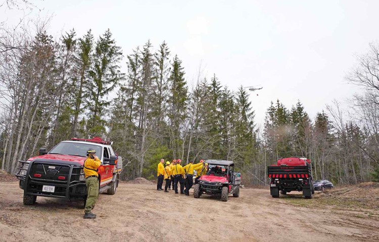 A Maine Forest Service helicopter flies above a firefighting crew near the scene of a large wildfire that burned overnight in Kennebunk. Officials said  the fire is more than 50 percent contained Thursday morning.