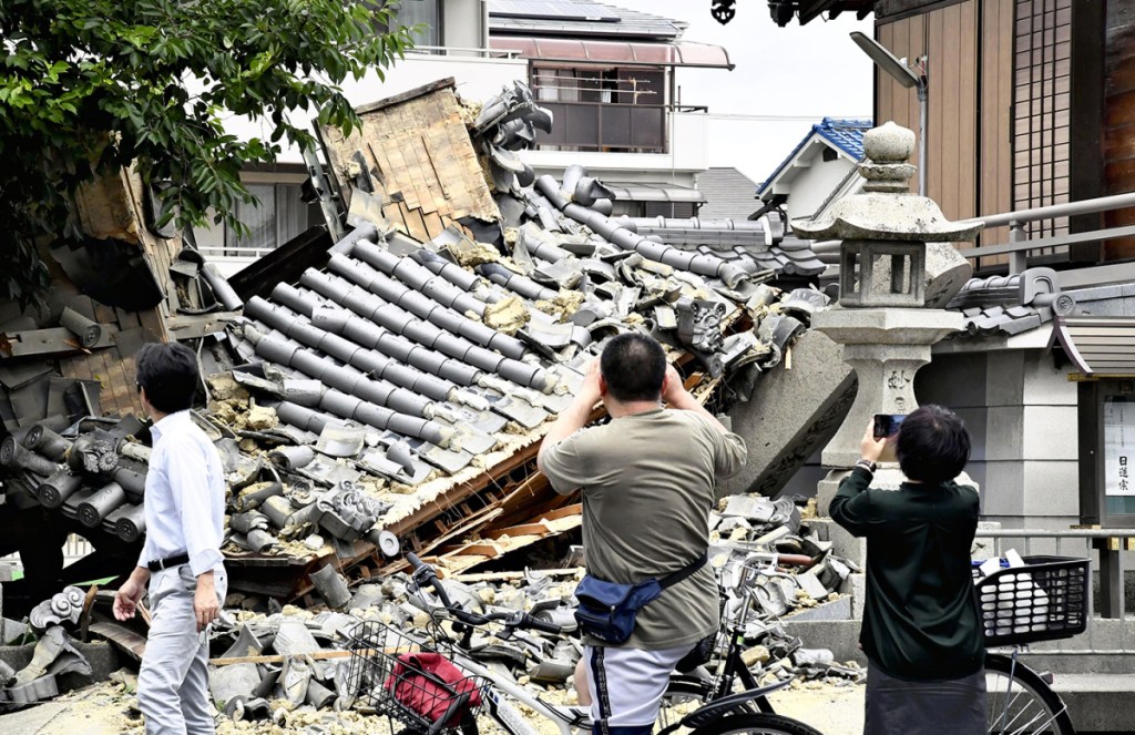 Residents photograph a temple gate in Ibaraki, Osaka Prefecture, that collapsed during the strong earthquake that hit western Japan shortly before 8 a.m. on Monday.