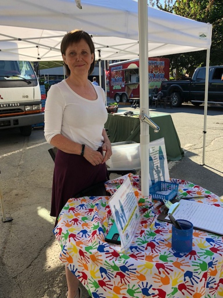 Elizabeth LaBua sets up a small table under an umbrella at the Downtown Waterville Farmers Market on Thursday to give people an opportunity to make a difference. She recruits volunteers to work at the homeless shelter.